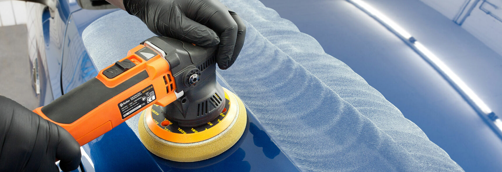 Eine Person poliert einen blauen Lack mit einer orangenen Poliermaschine.